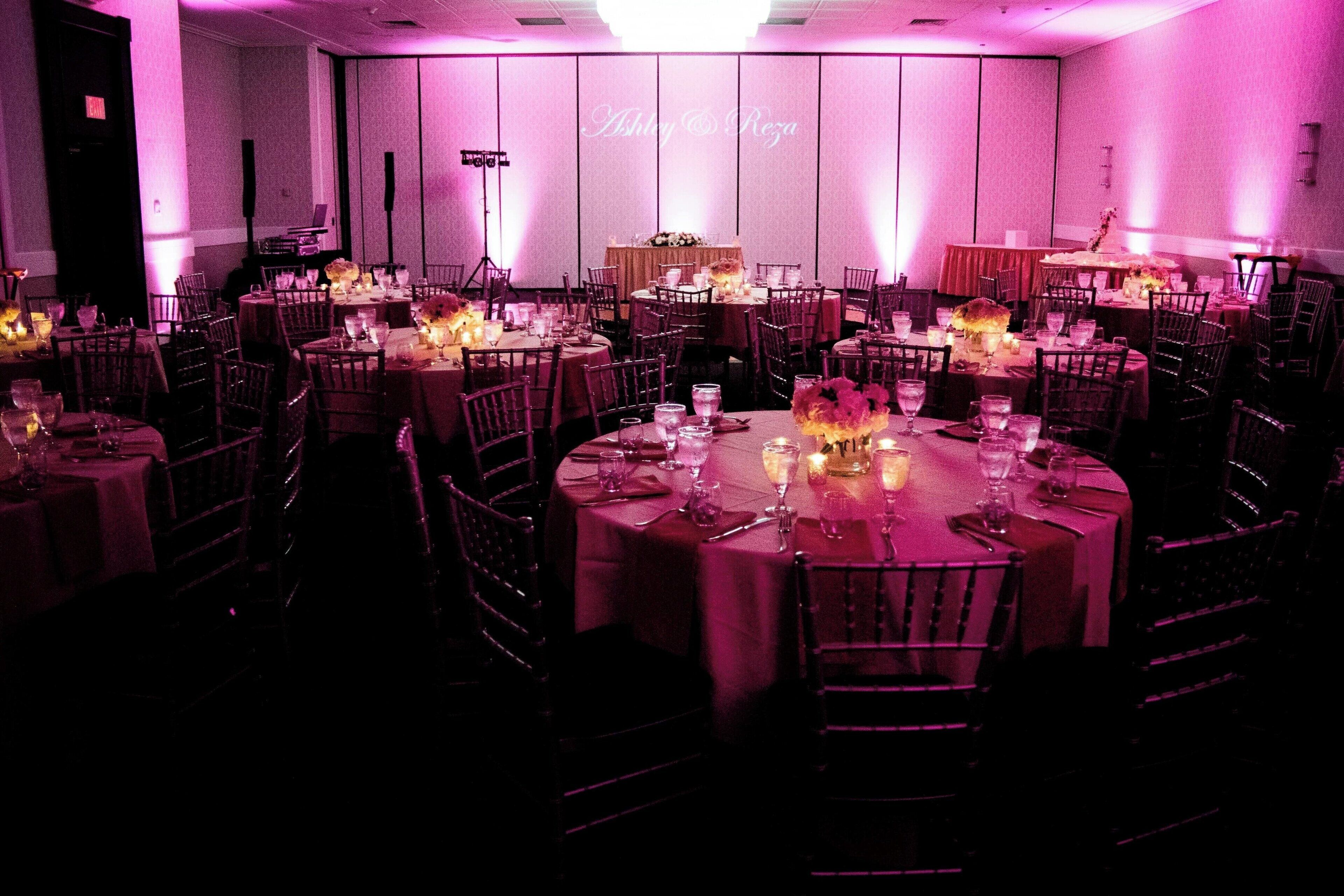 Uma sala de banquetes com mesas redondas dispostas para refeições, cada uma com velas e louças.