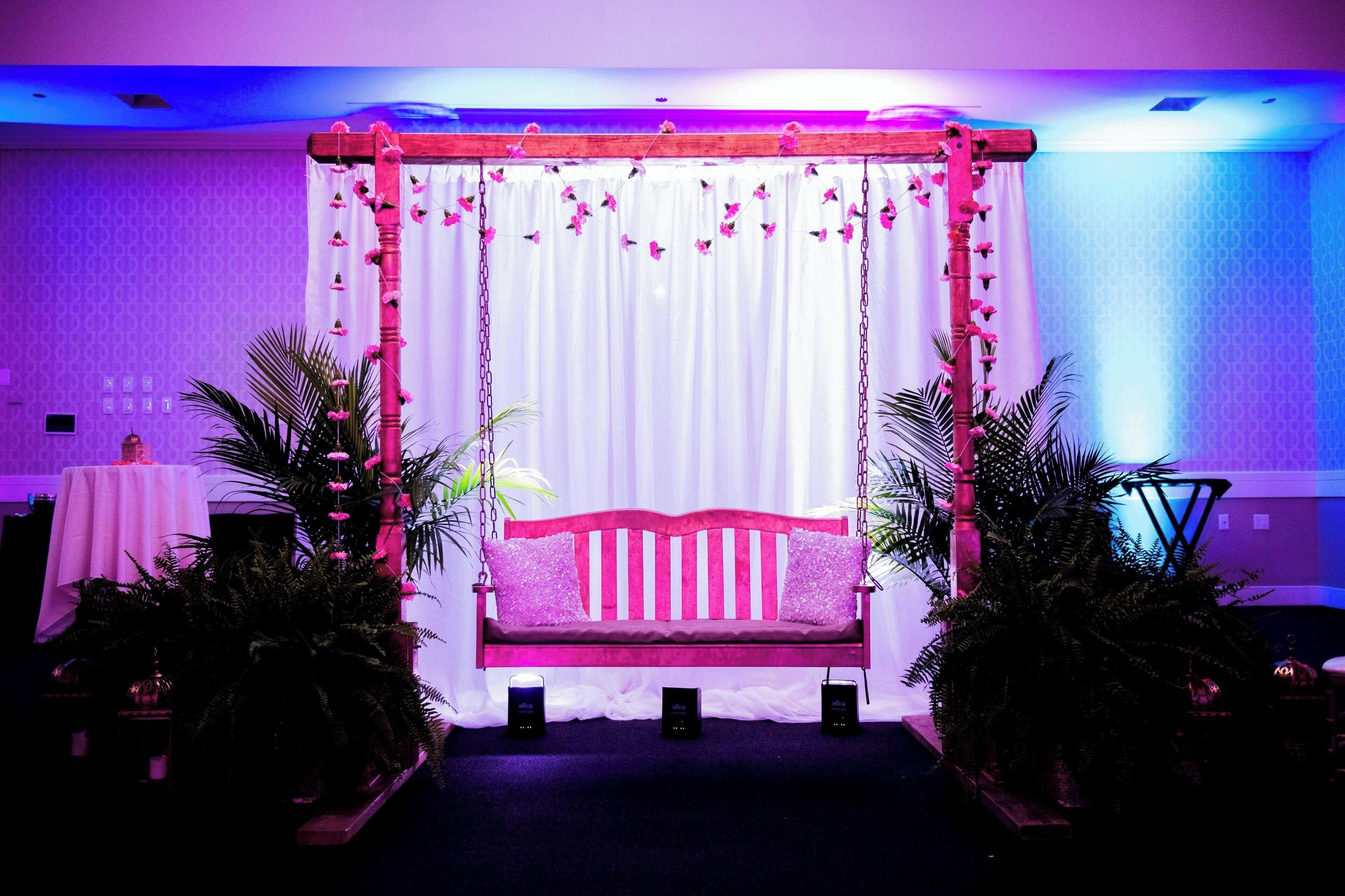 A stage with a pink swing set, white curtains, and floral decorations.