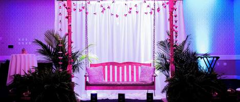 Un escenario con un columpio rosa, cortinas blancas y decoración floral.