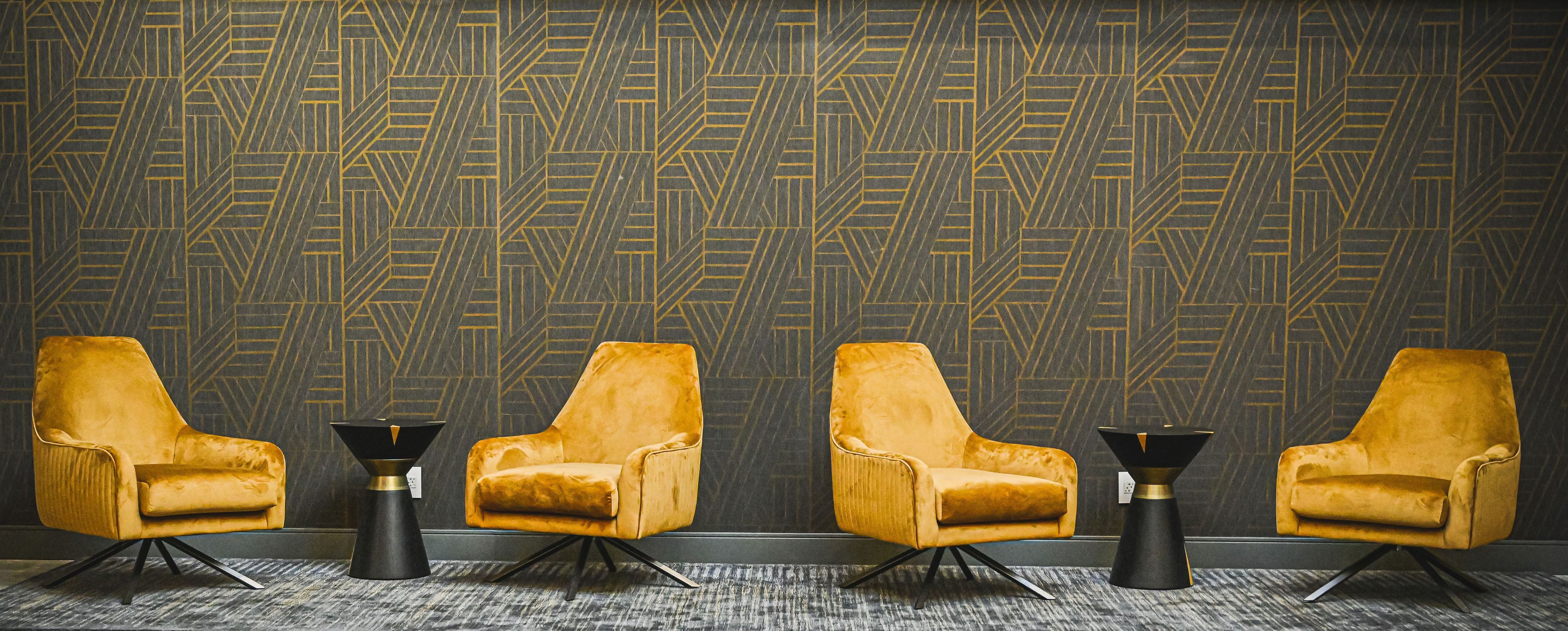 A room with four yellow velvet armchairs and three black and gold side tables.