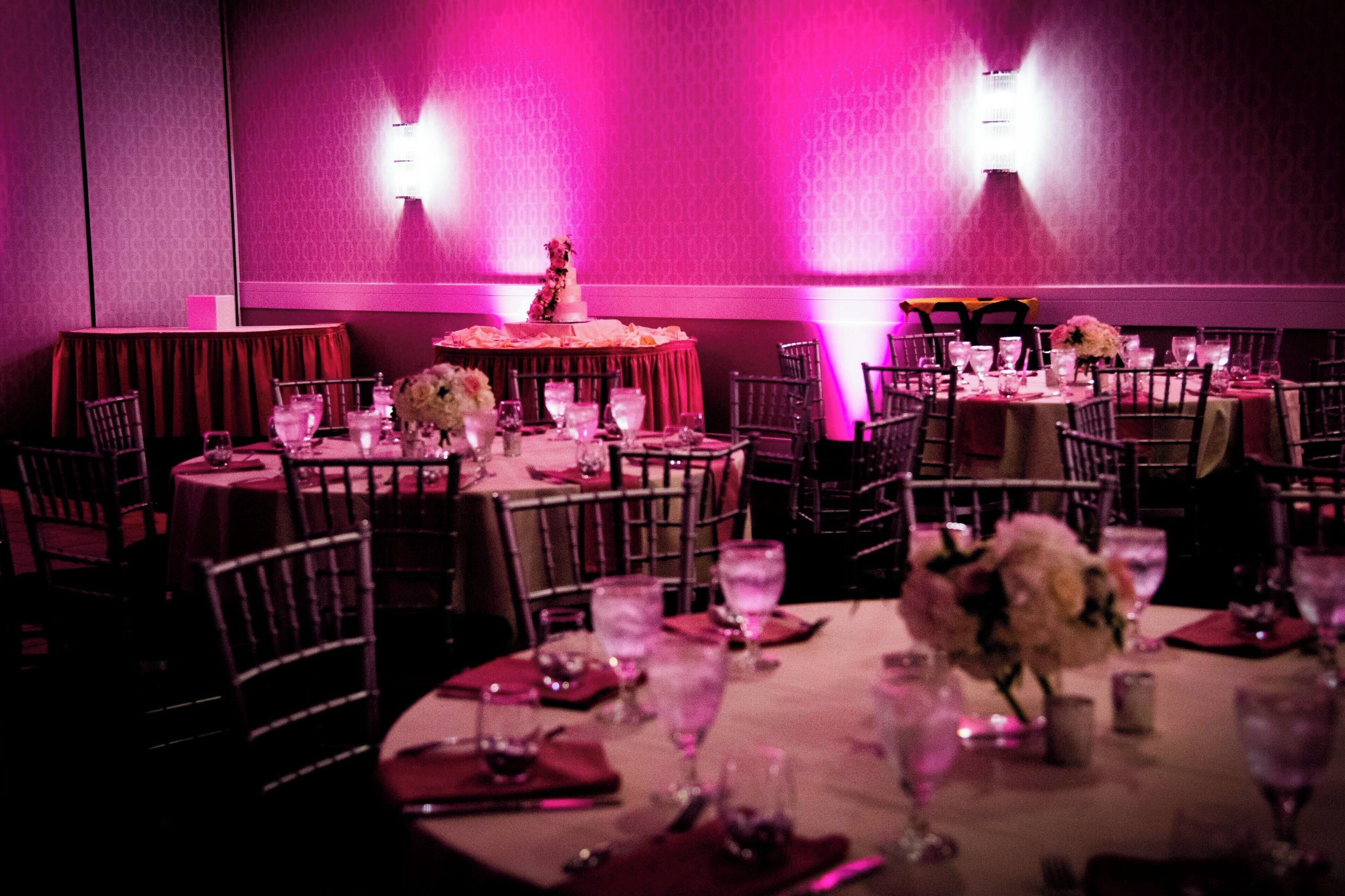 Un restaurant avec des tables rondes, des chaises et un éclairage rose.