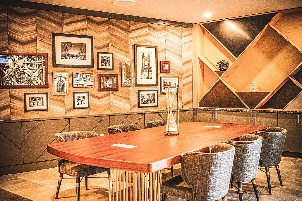 A conference room with a wooden table and chairs, framed pictures on the wall, and a geometric patterned wall design.