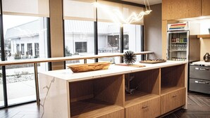 A modern kitchen with a marble countertop, wooden cabinets, and a view of the outside through large windows. - Delta Hotels by Marriott Cincinnati Sharonville (Sharonville)