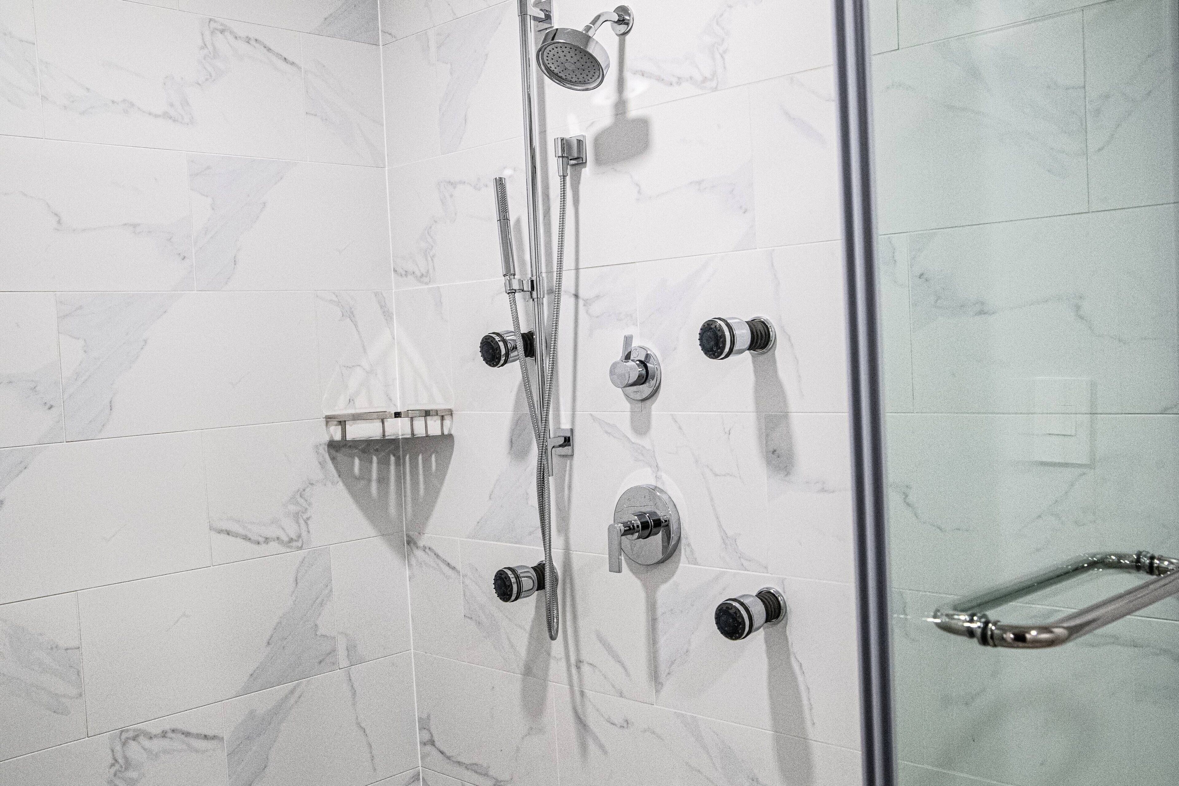 A shower area with a glass door, a handheld showerhead, a wall-mounted faucet, and a handheld shower attachment.