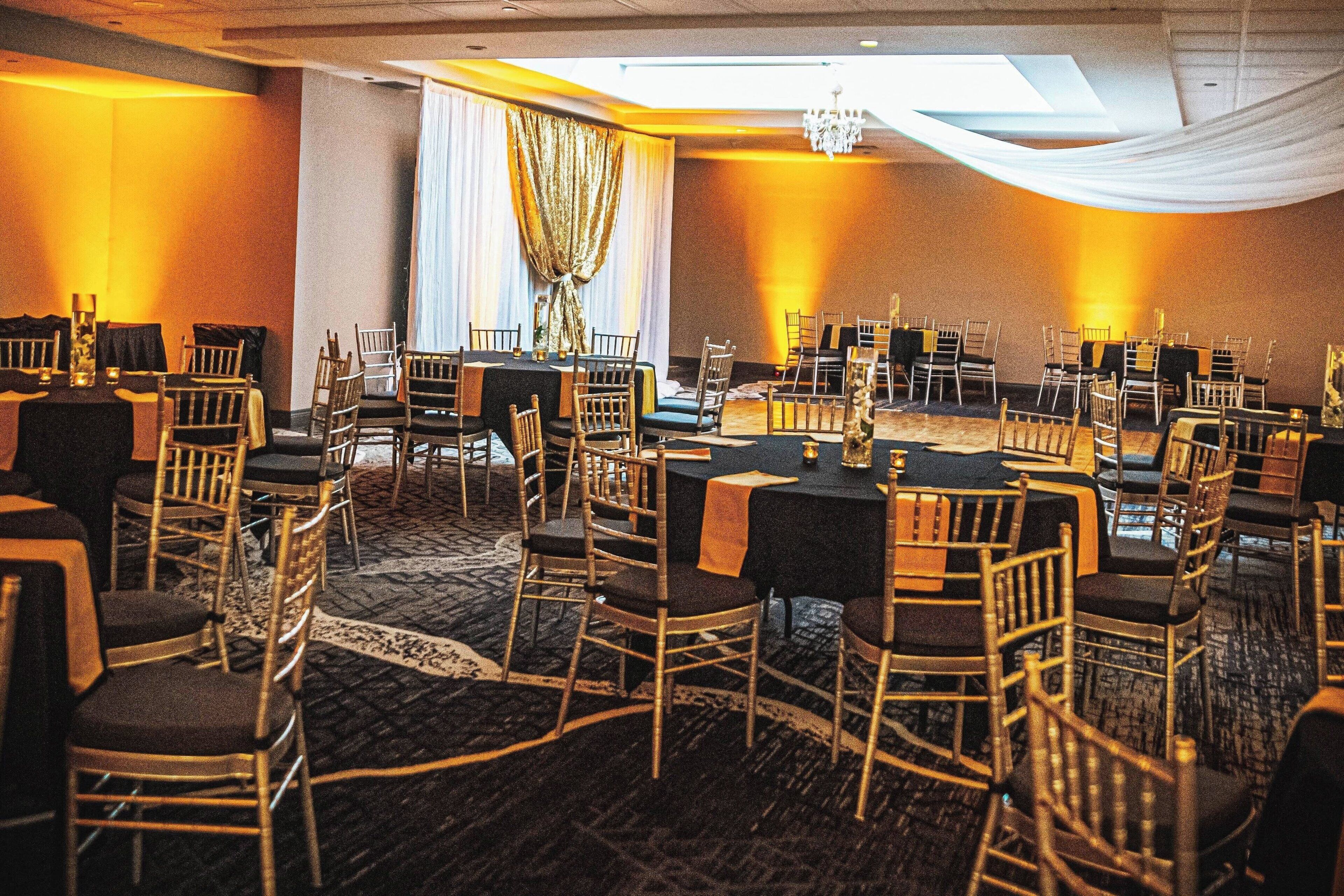Une salle de banquet avec des tables rondes et des chaises, un lustre et des rideaux tombants.