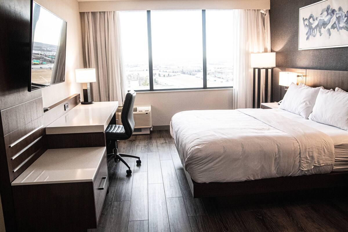 Une chambre d’hôtel équipée d’un lit, d’un bureau, d’une chaise et d’une grande fenêtre donnant sur la ville.