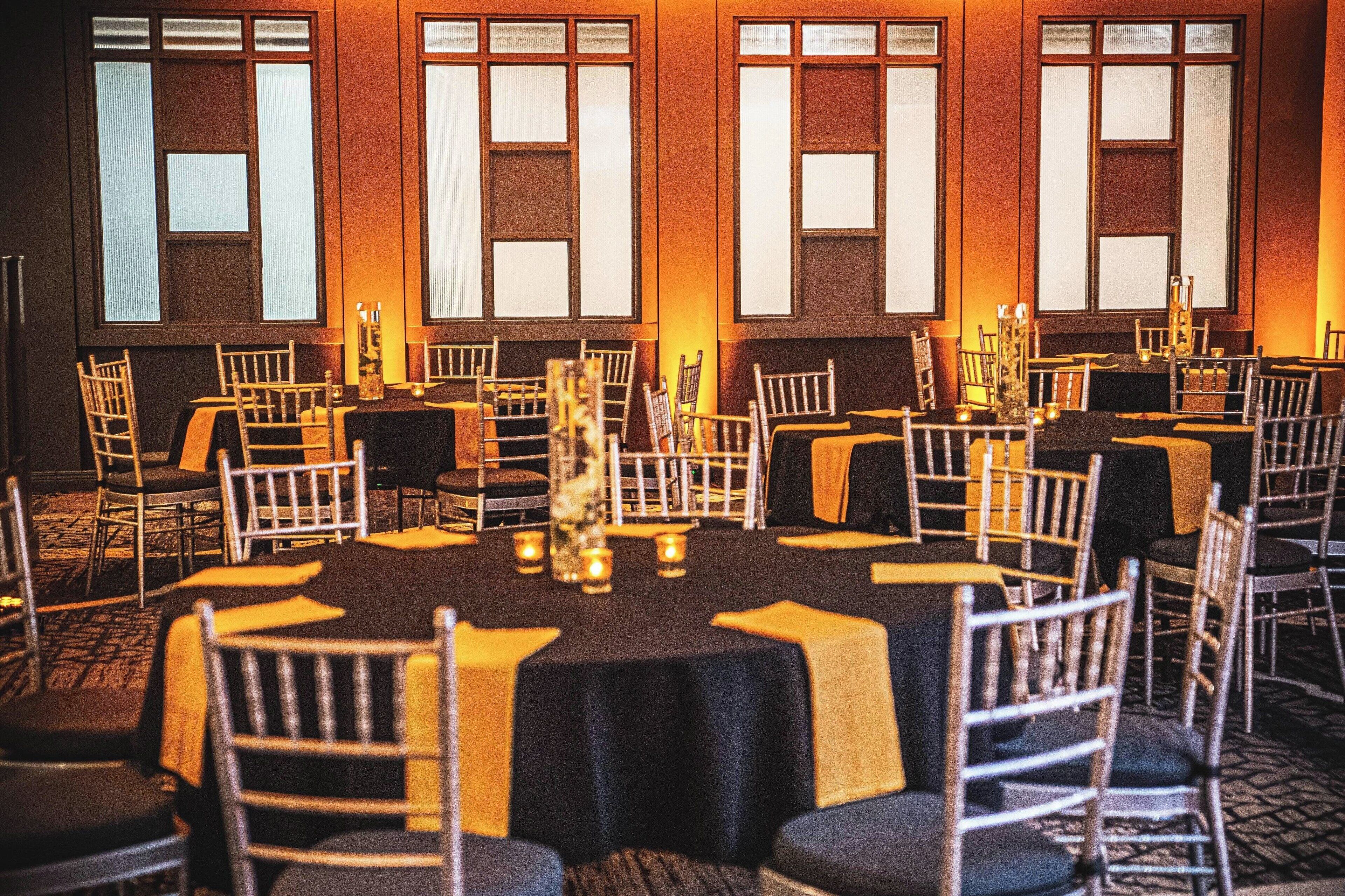 Une salle de banquet avec des tables rondes, des chaises et des centres de table décorés de bougies.