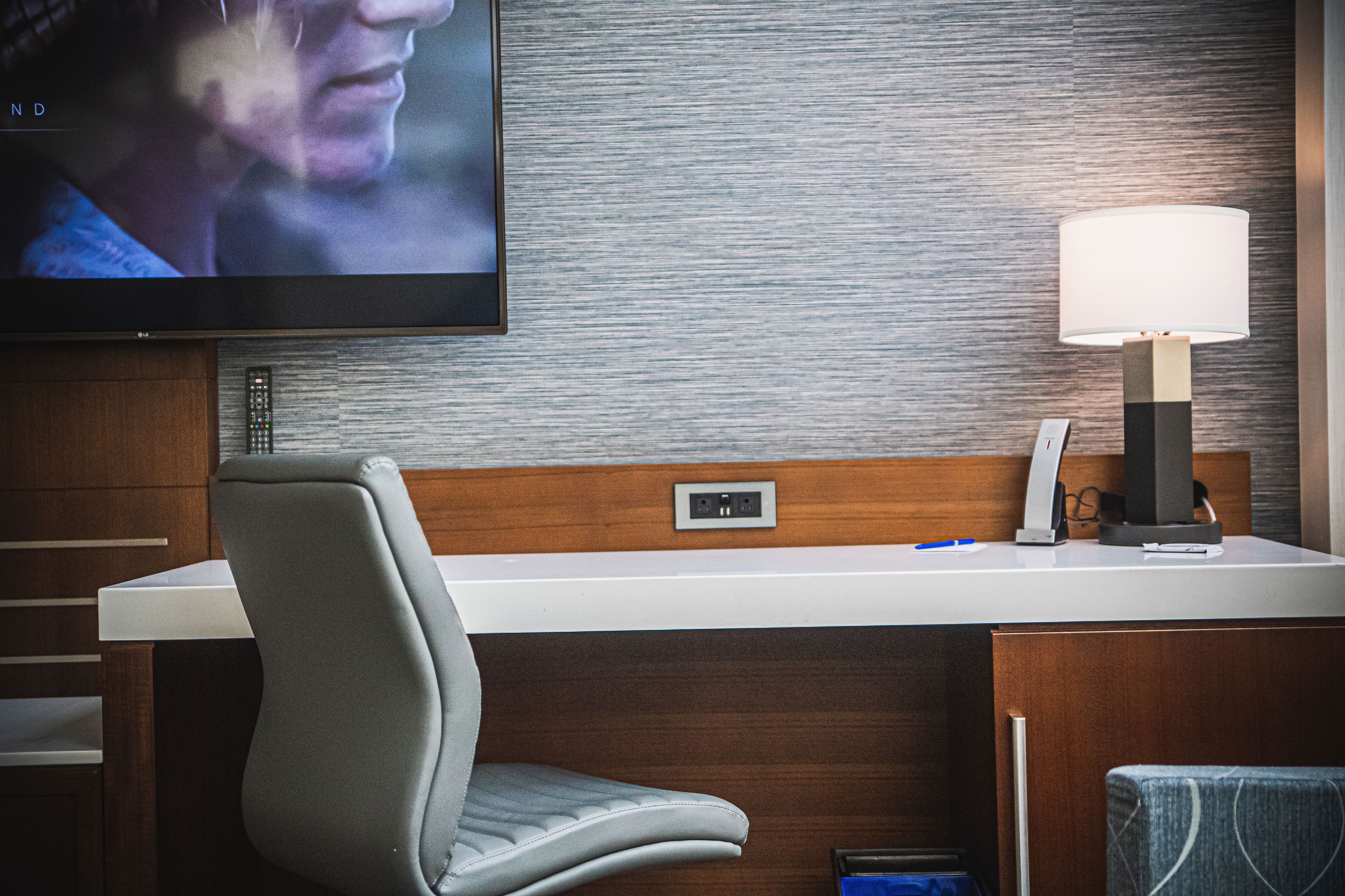 Une chambre d’hôtel équipée d’un téléviseur à écran plat fixé au mur, d’un bureau avec une lampe et d’une chaise.