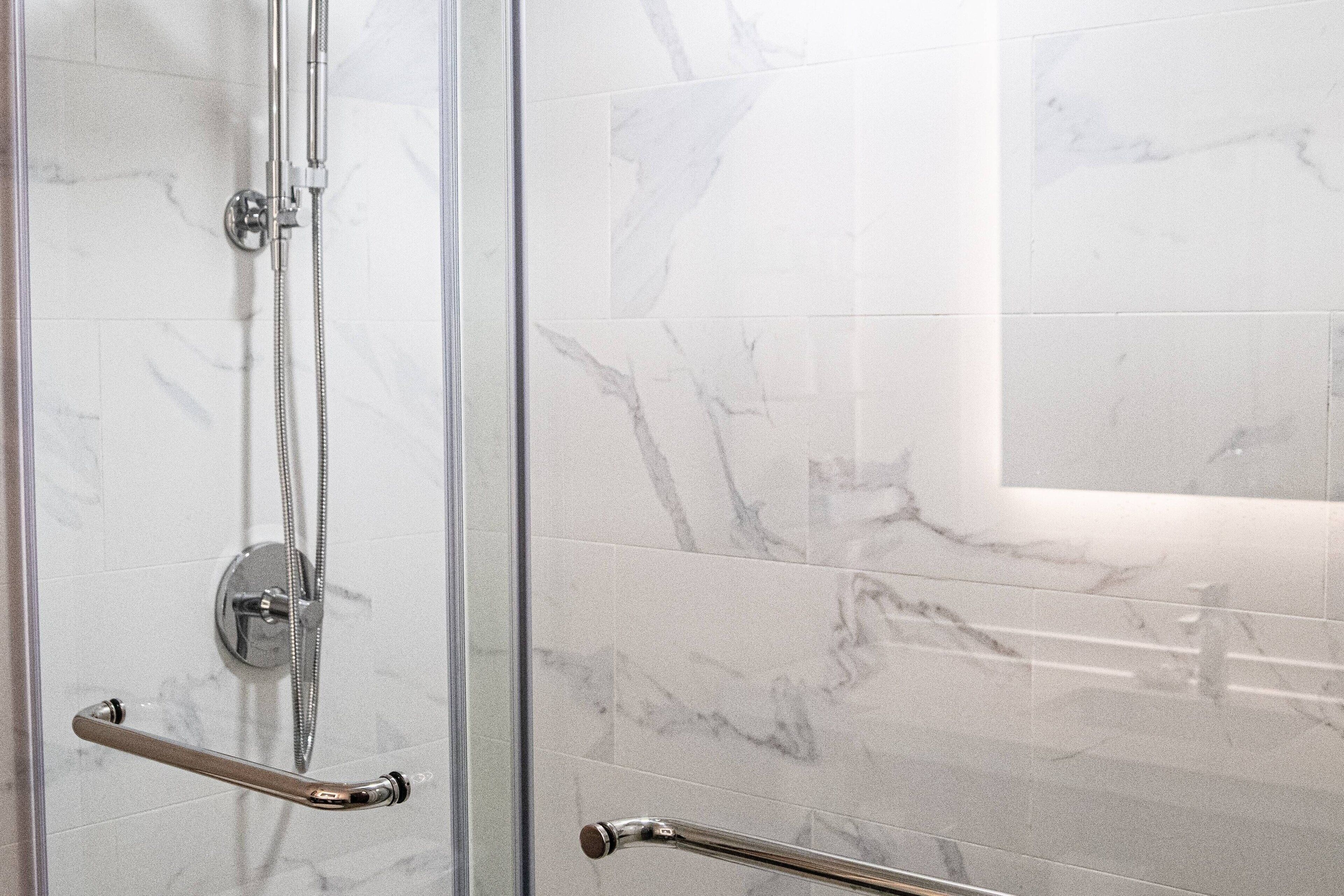 Een douchecabine met glazen wanden, een chromen handgreep en een handdouche.
