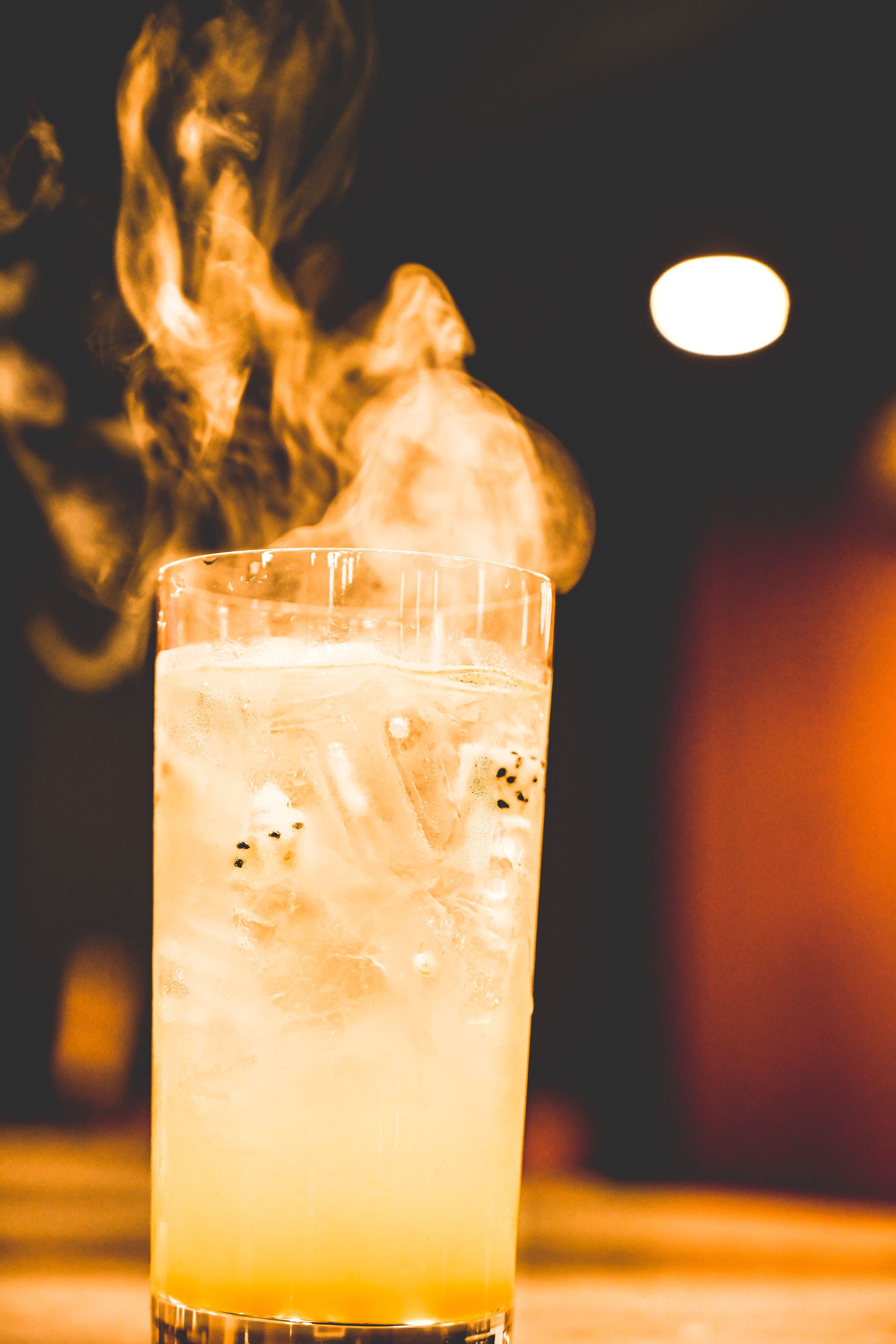 A glass of a clear beverage with ice cubes and a dark background.