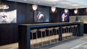 A modern bar area with a long counter, multiple bar stools, and overhead lighting.