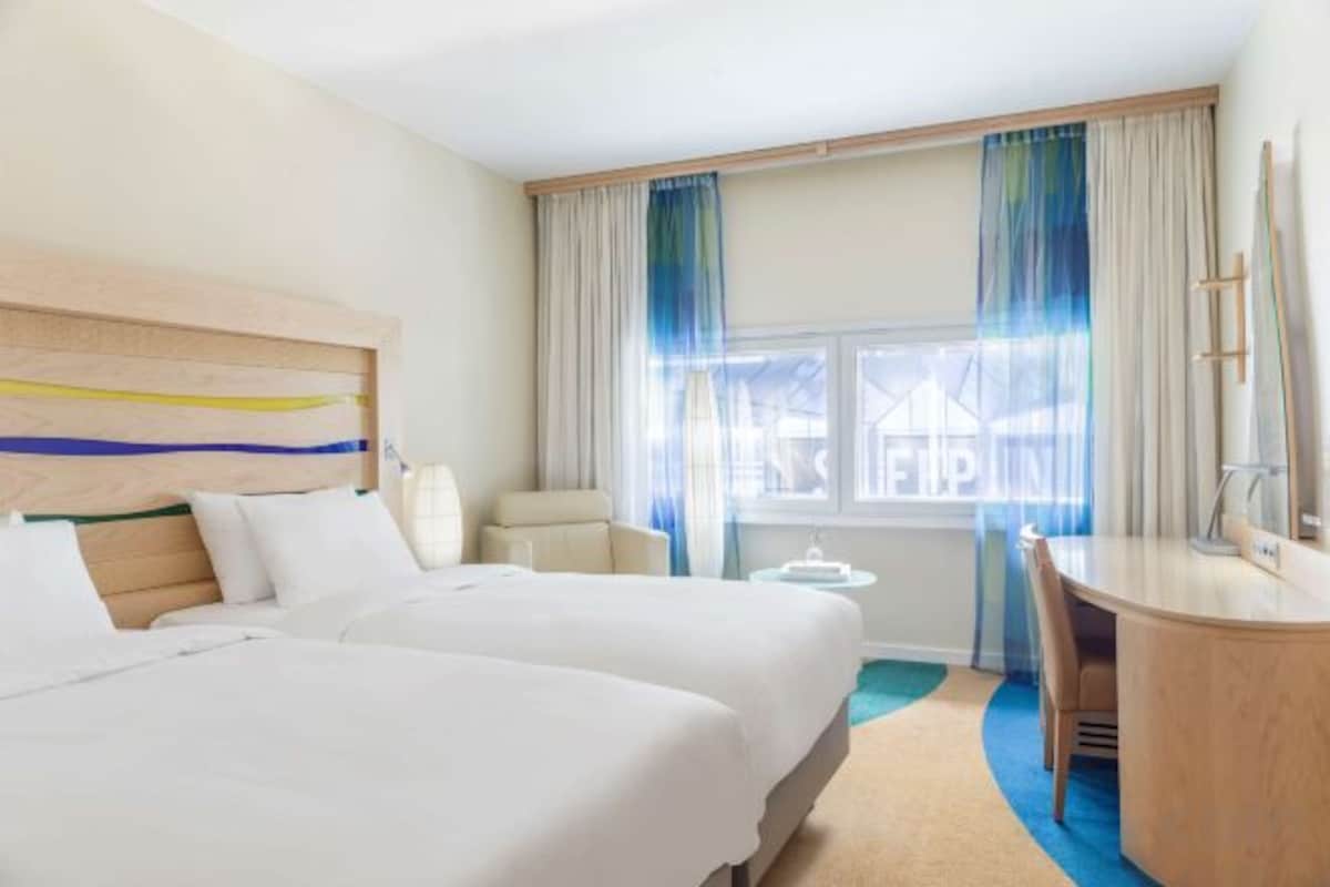 A hotel room with two beds, a desk, a chair, and a window with curtains.