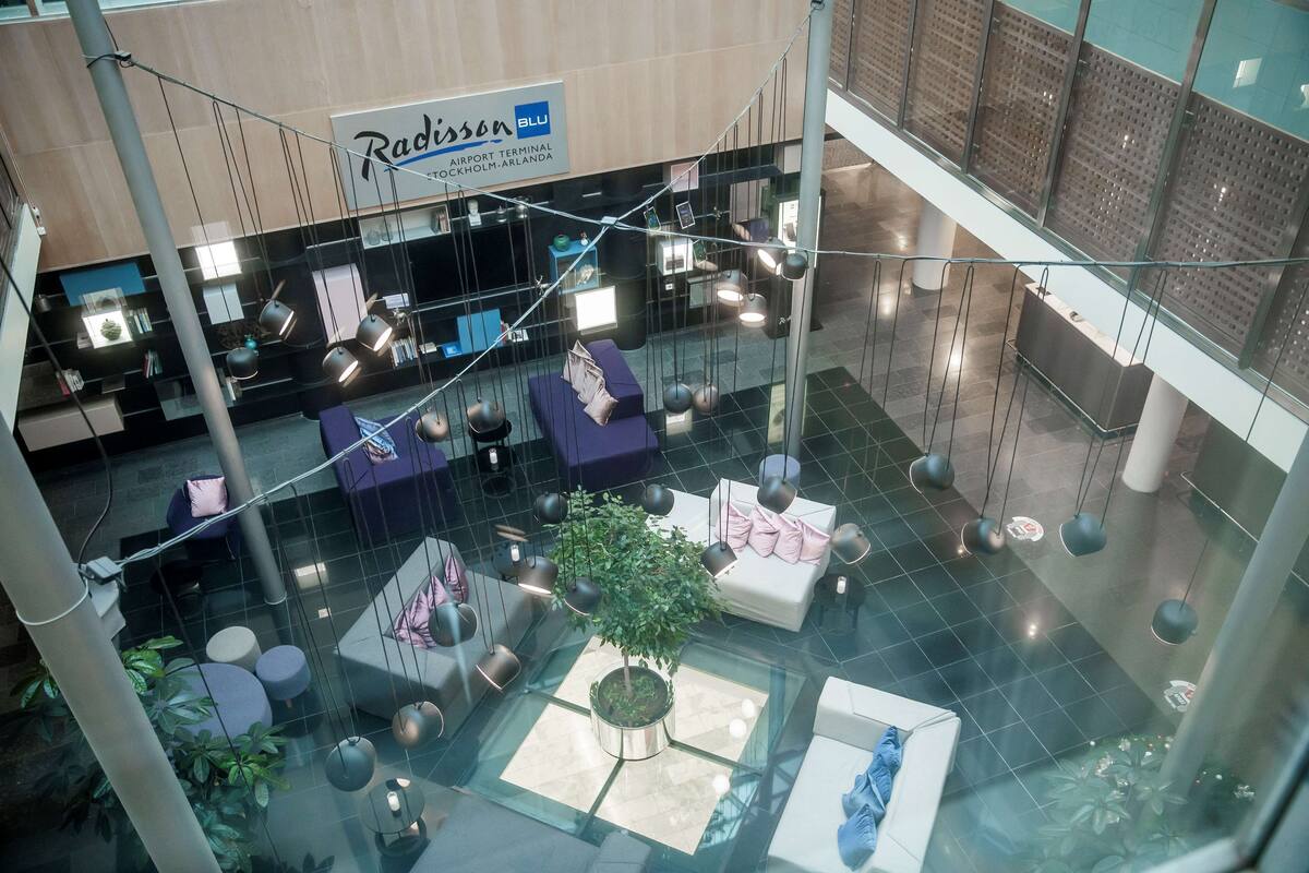 A spacious airport terminal with seating areas, a reception desk, and a sign for Radisson Blu.