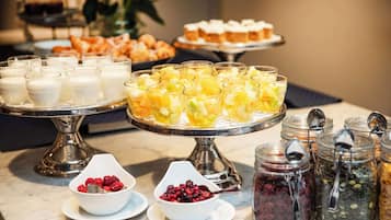 Un bufé con diversos alimentos, incluyendo copas de fruta, yogures y distintas variedades de untables.