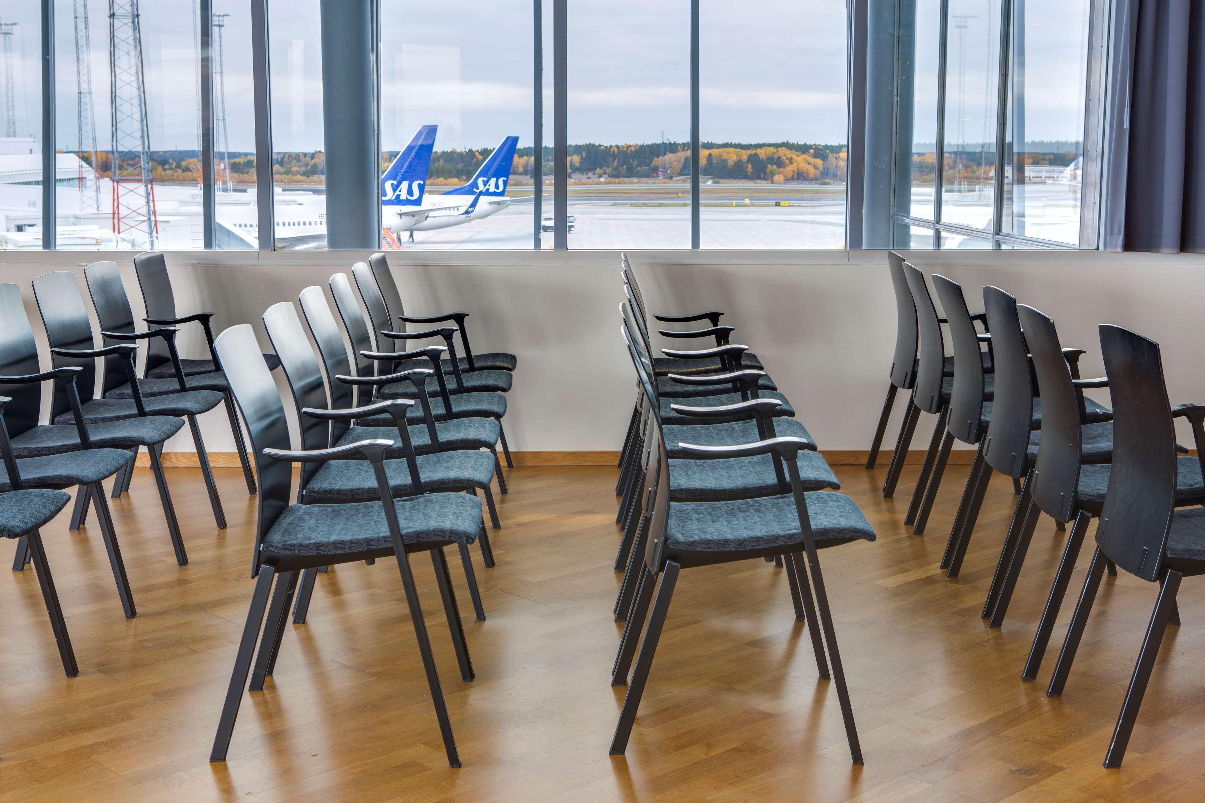Une rangée de chaises est placée face à une fenêtre d’où l’on peut voir un aéroport et un avion bleu.