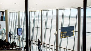 A modern airport terminal with large windows, a central information board, and a seating area.