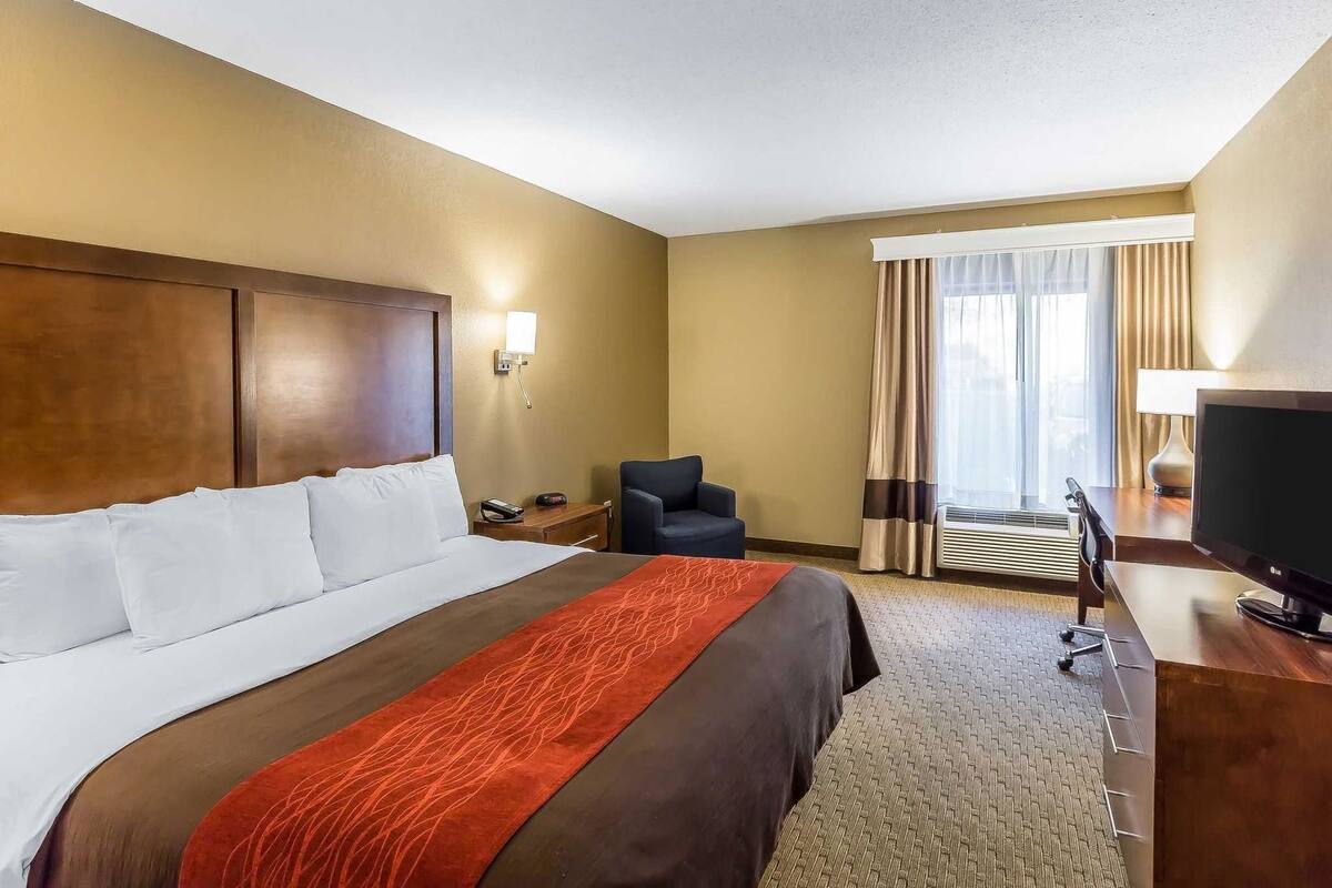 A hotel room with a large bed, a desk with a TV, a chair, and a window with curtains.