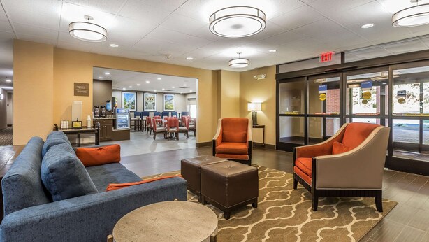 A hotel lobby with a blue sofa, orange armchairs, a coffee station, and a reception desk.