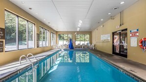 An indoor swimming pool with clear windows, a lifeguard chair, and exit signs.