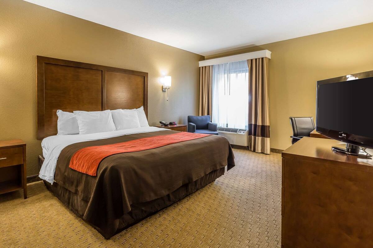 A hotel room with a large bed, a desk with a television, a chair, and a window with curtains.