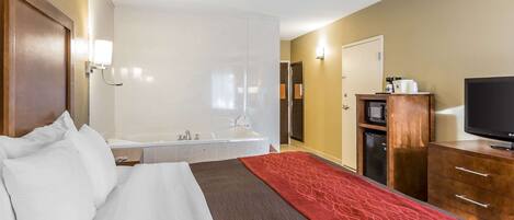 A hotel room with a bed, a red decorative rug, a television, a desk with a computer, and a bathroom with a bathtub.