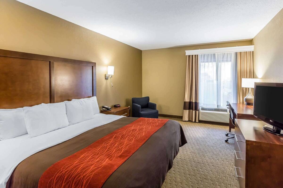 A hotel room with a large bed, a desk with a television, a chair, and a window with curtains.