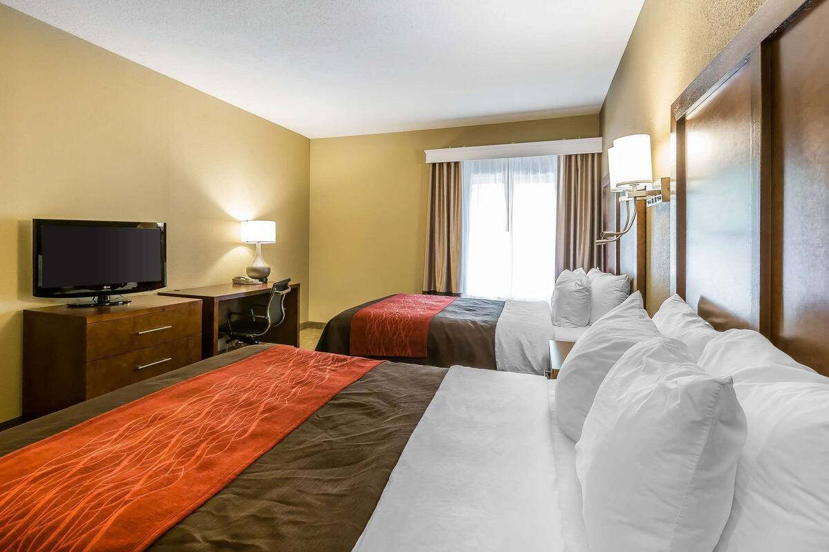 A hotel room with two beds, a desk with a television, a lamp, and a window with curtains.
