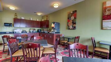 A dining area with wooden chairs and tables, a kitchen with wooden cabinets, and a microwave on the counter.