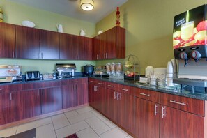 A kitchen with wooden cabinets, a coffee machine, a fruit juice dispenser, and various kitchen appliances. - Red Roof Inn Springfield, OH (Springfield)