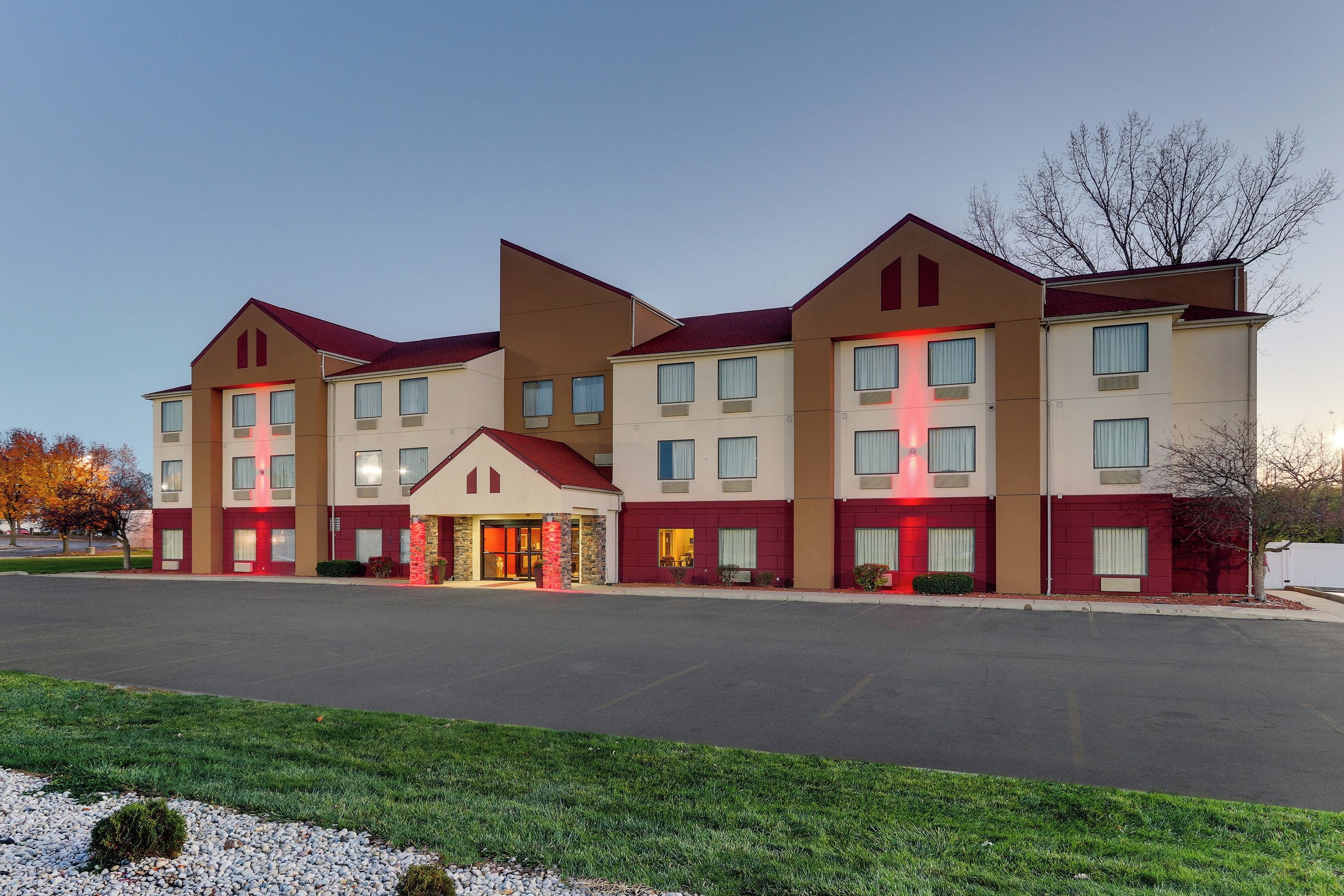 A multi-story hotel with a central entrance, multiple windows, and a parking lot in front.