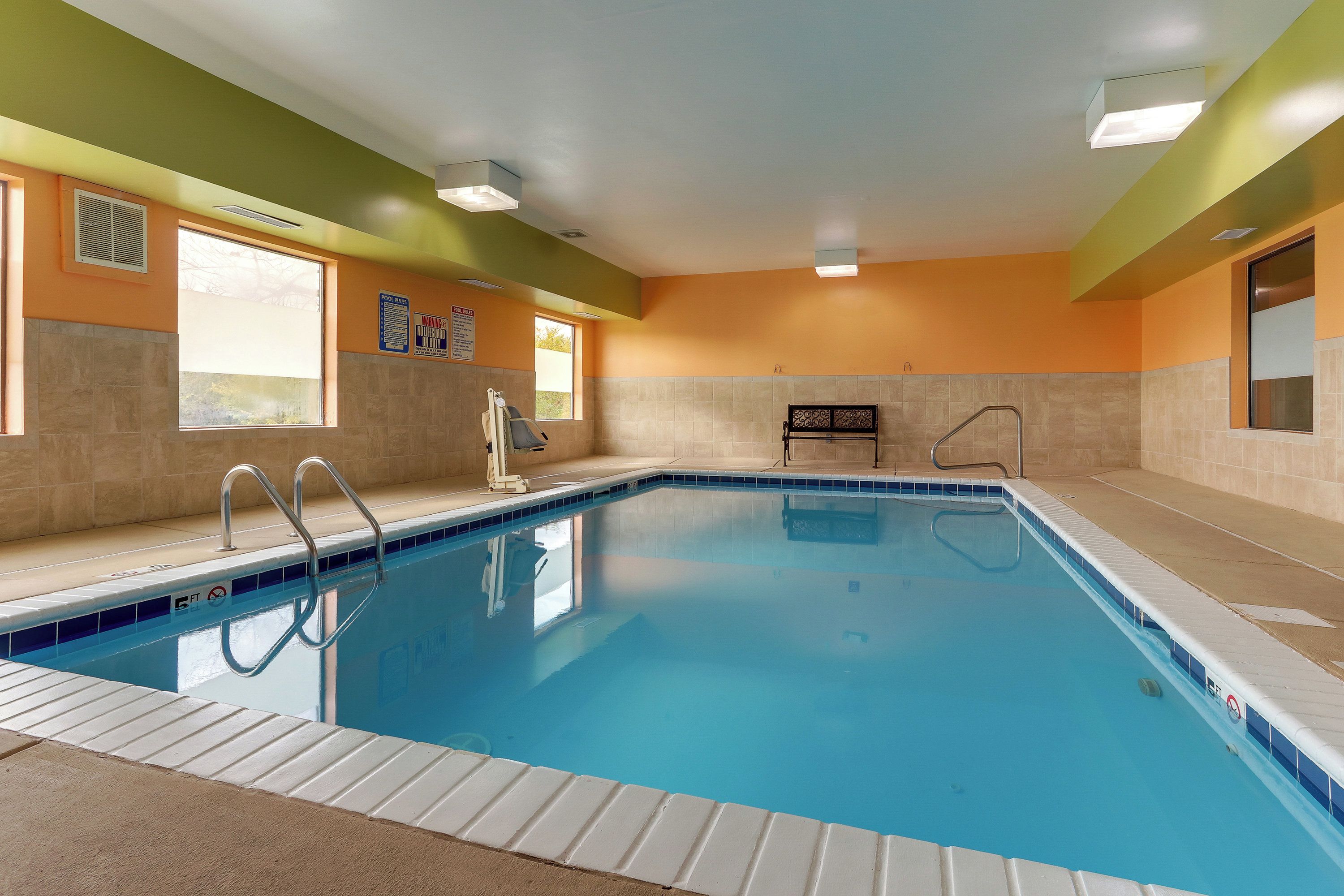 Una piscina interior con agua cristalina, un trampolín y un cartel que indica las normas de la piscina.