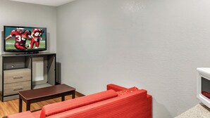 A living room with a flat-screen TV on a stand, a brown bench, and a red sofa.