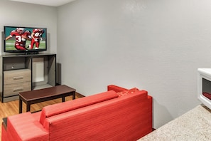 Una sala de estar con un televisor de pantalla plana sobre un mueble bajo, un banco marrón y un sofá rojo.