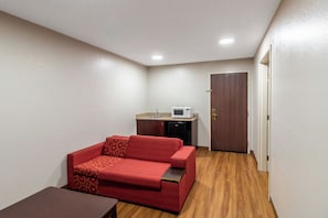Habitación compacta con sofá rojo, kitchenette pequeña y piso de madera.