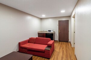 Quarto compacto com sofá vermelho, pequena cozinha e piso de madeira.