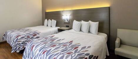 A hotel room with two beds, a nightstand, a lamp, and a chair.