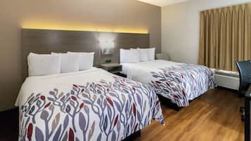 A hotel room with two beds, a nightstand, a wall-mounted lamp, an air conditioning unit, and a curtain.