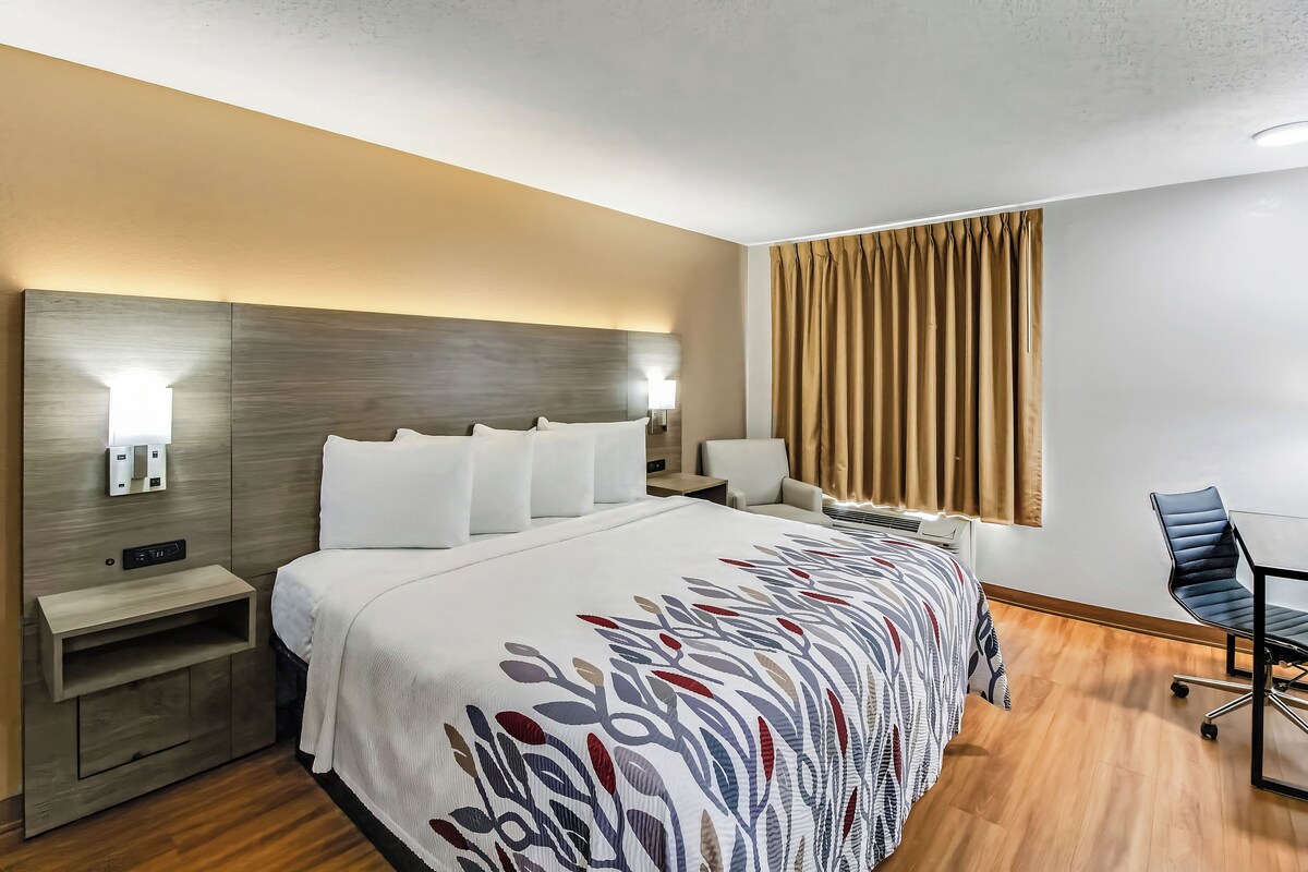 A hotel room with a bed, bedside tables, a desk, a chair, and a window with curtains.