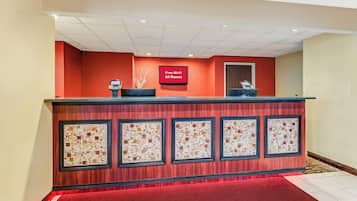 A reception desk with a digital display, a red carpet, and a wall with framed artwork.
