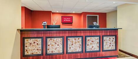 A reception desk with a digital display, a red carpet, and a wall with framed artwork.