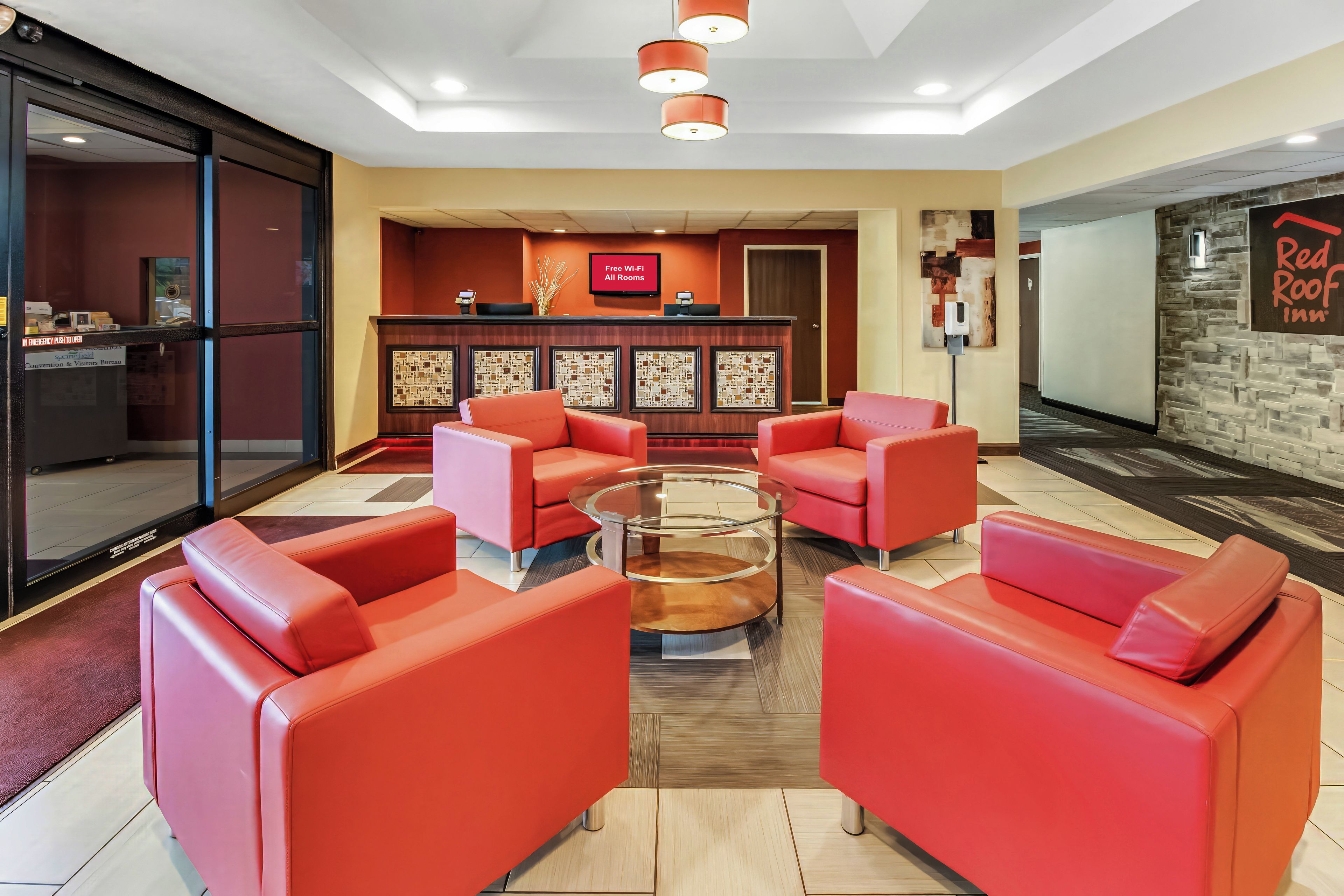 Un vestíbulo con sofás de cuero rojo, una mesa de centro de vidrio y un mostrador de recepción con un cartel que dice 'Wi-Fi gratuito en todas las habitaciones'.
