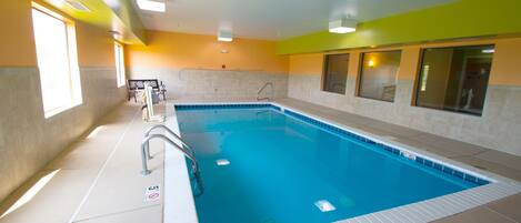 An indoor swimming pool with clear water, a diving board, and a lifeguard chair.