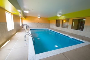 An indoor swimming pool with clear water, a diving board, and a lifeguard chair.