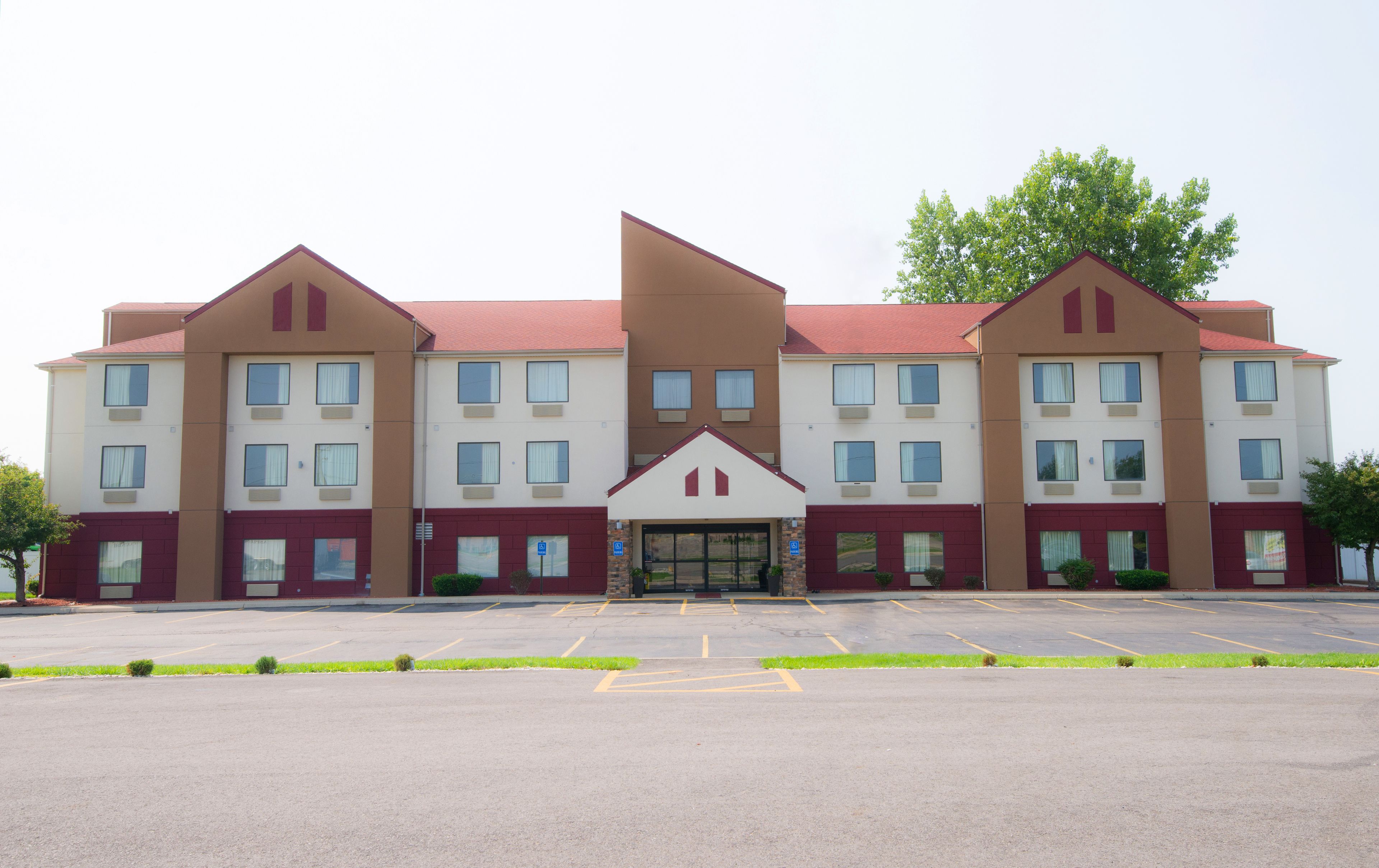A multi-story hotel with a symmetrical facade, a central entrance, and a parking lot in front.