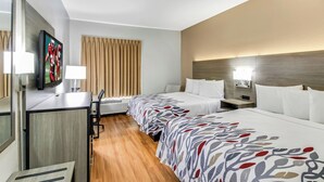 A hotel room with a desk, two beds, a television, and a window with curtains.