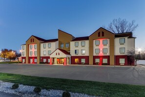 A multi-story hotel with a central entrance, multiple windows, and a parking lot in front.