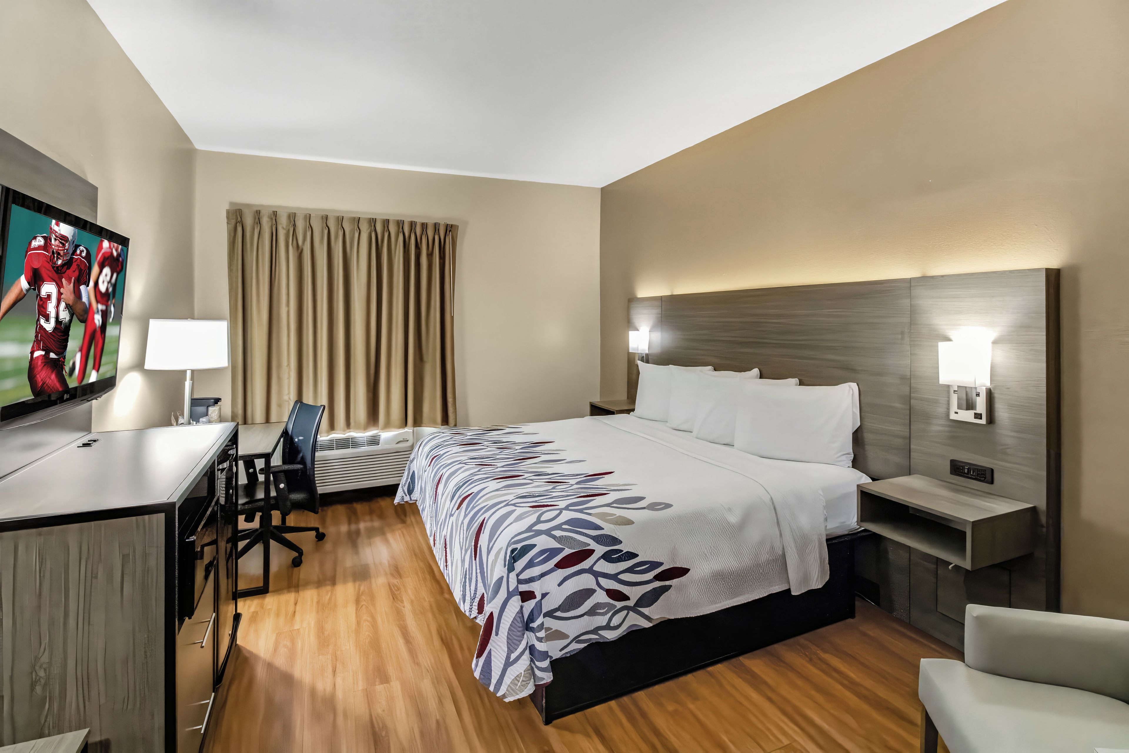A hotel room with a bed, desk, chair, television, and a window with curtains.