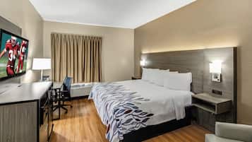 A hotel room with a bed, desk, chair, television, and a window with curtains.