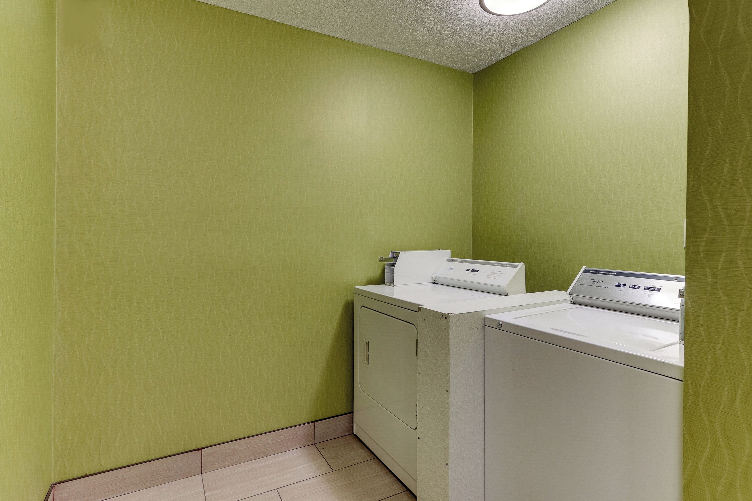 A laundry room with a washing machine and dryer, green walls, and a tiled floor.