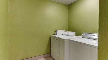 A laundry room with a washing machine and dryer, green walls, and a tiled floor.